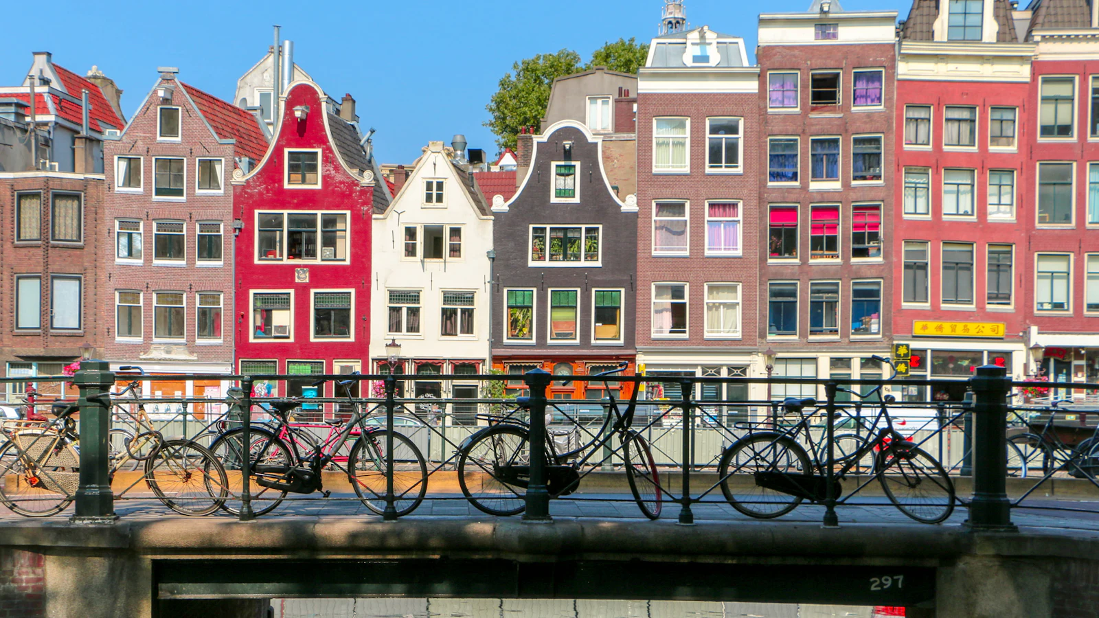 Des vélos sur un pont au-dessus d'un canal d'Amsterdam bordé de maisons à pignons